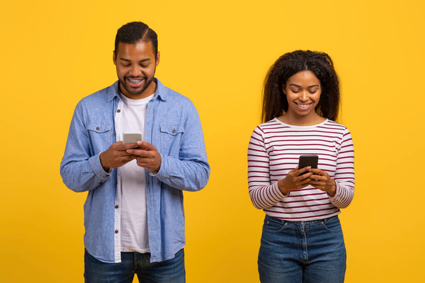 Afrikkalainen amerikkalainen mies ja nainen katsovat tarkasti kännykkäruutua. He seisovat lähellä toisiaan, molemmat keskittyivät laitteeseen - Valokuva, kuva