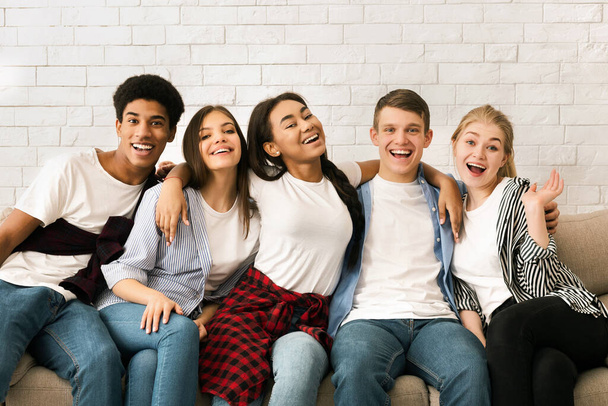 A group of multiracial teenagers, guys and girls, are seated on top of a large couch. They seem engaged in conversation or watching something together. - Photo, Image