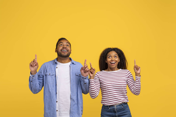 A young African American man and woman stand side by side, looking up with expressions of surprise and excitement, both pointing upwards, copy space - Photo, Image
