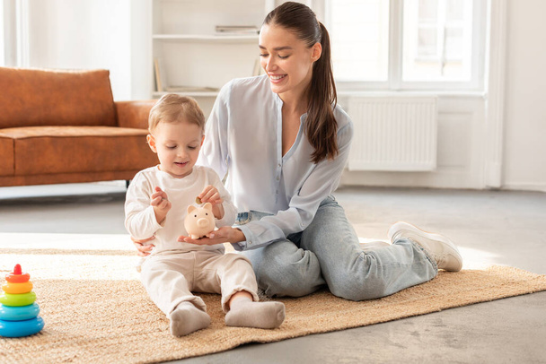Una mujer está sentada en el suelo, jugando con un bebé. Ella está interactuando con el bebé de una manera nutritiva, estimulando su desarrollo a través de la comunicación táctil y verbal - Foto, Imagen