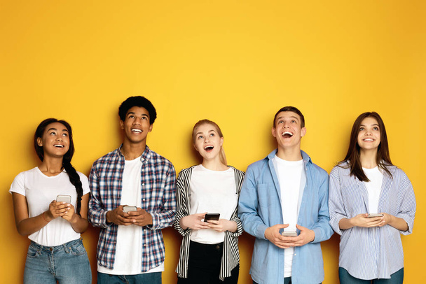 Un momento alegre compartido entre un grupo multiétnico de adolescentes, todos mirando hacia arriba y riendo con genuina felicidad. - Foto, imagen