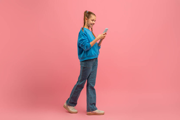 Een jong meisje met een blauw shirt is gericht op haar mobiele telefoon scherm in dit openhartige moment vastgelegd in een openbare omgeving. Ze lijkt in beslag genomen door haar telefoon, mogelijk sms 'en of scrollen. - Foto, afbeelding