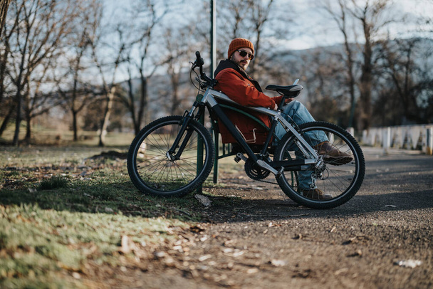Человек в повседневной одежде наслаждается спокойным моментом на велосипеде в спокойной обстановке парка. - Фото, изображение