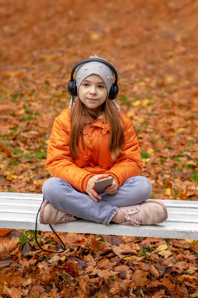 Дівчина слухає музику на навушниках в осінньому парку і дивиться на камеру - Фото, зображення