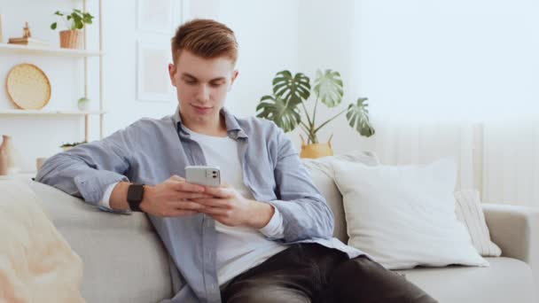 Moderne communicatie. Millennial guy chatten op mobiele telefoon met vrienden, surfen web thuis - Video