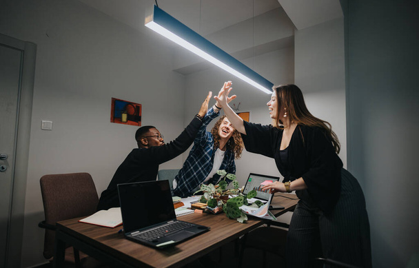 Joyful collega 's delen een high-five in een kantoor, het weergeven van teamwork en succes met computers en papierwerk rond. - Foto, afbeelding