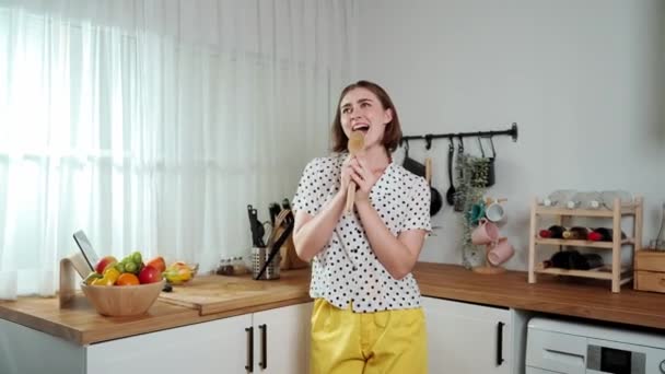 Energetic caucasian mother singing by holding ladle at modern kitchen while cooking and making salad for breakfast. Happy house keeper moving to music while prepare for making healthy food. Pedagogy. - Footage, Video