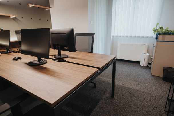 Tilava ja valoisa toimisto, jossa on kaksi tietokonenäyttöä suurella puupöydällä, minimalistinen sisustus ja mukava työtilan tunnelma. - Valokuva, kuva
