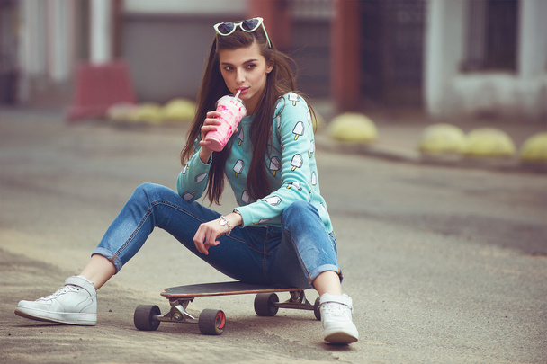 mooie jonge vrouw poseren met een skateboard, mode levensstijl bij zonsondergang - Foto, afbeelding