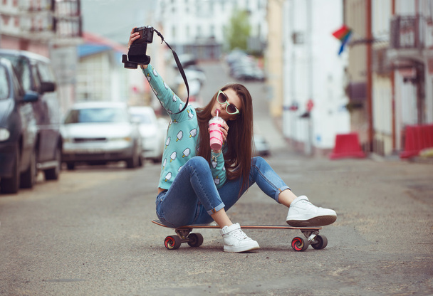 mooie jonge vrouw poseren met een skateboard, mode levensstijl bij zonsondergang - Foto, afbeelding