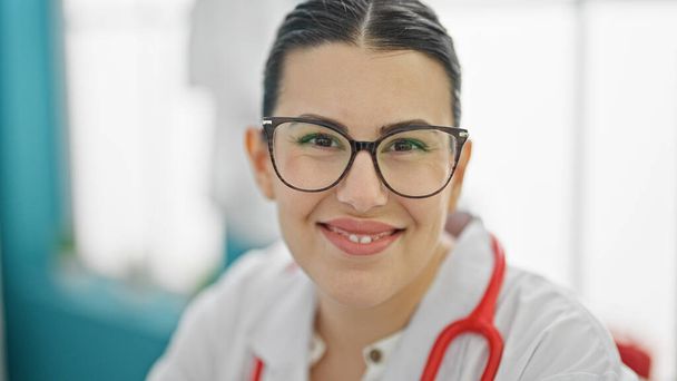 Jovem bela mulher hispânica médico sorrindo confiante na clínica - Foto, Imagem