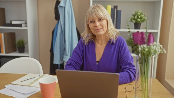 Une femme d'âge moyen confiante qui travaille sur un ordinateur portable dans un bureau à domicile moderne avec un beau décor. - Photo, image