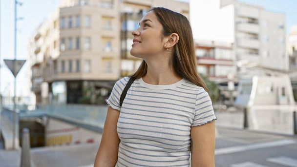 Jeune femme souriante aux cheveux longs profitant de sa journée dans un cadre urbain dynamique, reflétant le mode de vie urbain et le bonheur. - Photo, image