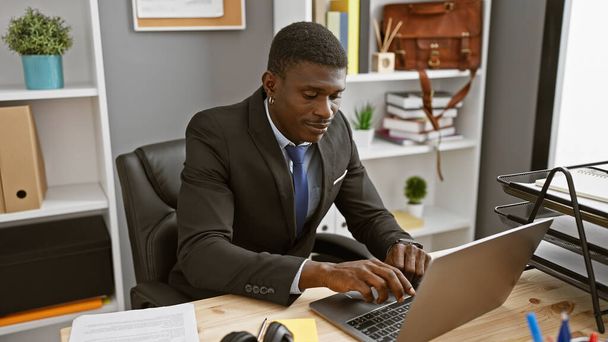 Όμορφος Αφροαμερικάνος επιχειρηματίας που εργάζεται σε ένα φορητό υπολογιστή σε ένα σύγχρονο περιβάλλον γραφείου. - Φωτογραφία, εικόνα