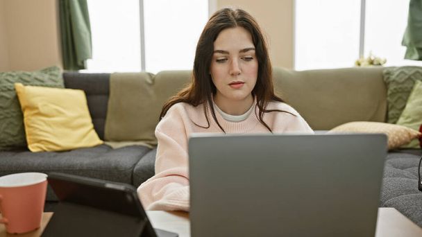 Keskittynyt nuori nainen käyttää kannettavaa tietokonetta viihtyisässä olohuoneessa sisustus - Valokuva, kuva