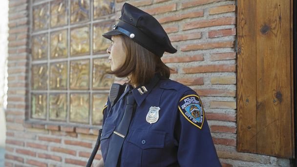 Un ufficiale donna matura sta vicino a un muro di mattoni, simboleggiando le forze dell'ordine in un ambiente urbano. - Foto, immagini