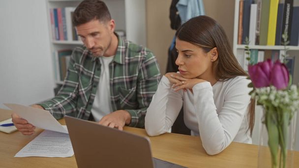Una pareja hispana preocupada revisa documentos en su oficina en casa, reflejando relación y planificación financiera. - Foto, imagen