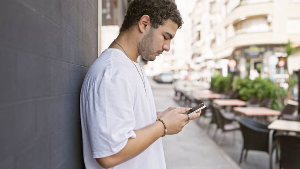 Молодой человек с бородой с помощью смартфона на солнечной улице города  - Фото, изображение