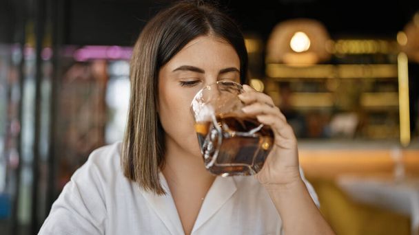 Young beautiful hispanic woman drinking a glass of vermouth at the restaurant - Photo, Image