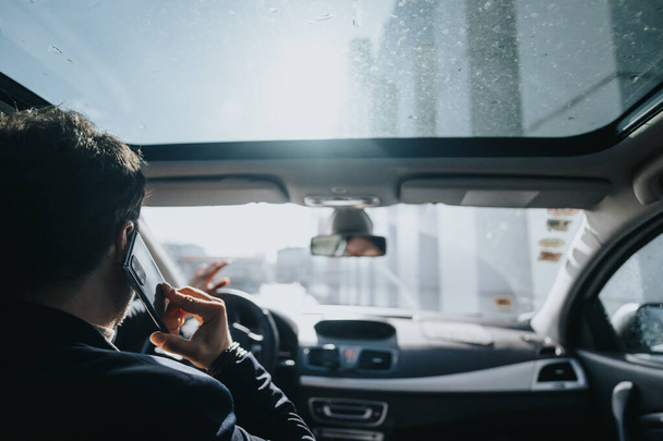 Vue arrière d'un homme en costume faisant un appel téléphonique sur le siège arrière d'une voiture, avec une lumière du jour brillante venant par la fenêtre. - Photo, image