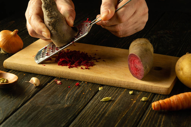 Een rasp in de hand van een kok voor het raspen van bieten. Concept van het koken van groenten gezonde schotel op keukentafel voor lunch. - Foto, afbeelding