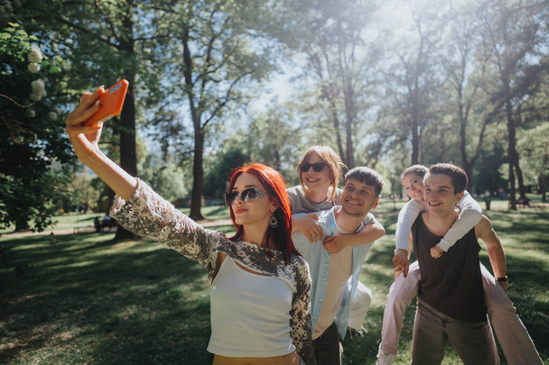 Adultos jóvenes muy alegres tomando una selfie de grupo en un parque iluminado por el sol. La imagen captura su felicidad y estrecha amistad durante un hermoso día. - Foto, Imagen