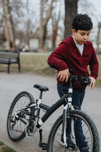 Un niño pequeño parece alegre y activo mientras monta su bicicleta en un entorno de parque, centrándose en el camino por delante. - Foto, Imagen