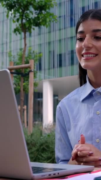 Dizüstü bilgisayar kullanan mutlu genç bir kadın ofis binasının ya da kampüs üniversitesinin önünde görüntülü arama yapıyor. - Video, Çekim
