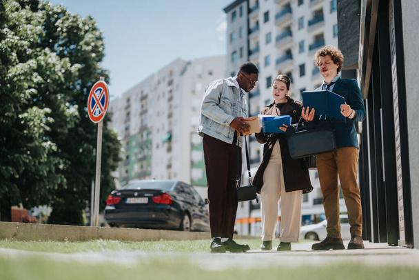 Three professionals engaged in a business meeting outdoors, holding documents and discussing actively with urban environment in background. - Photo, Image