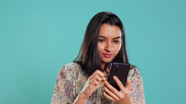 Mujer felizmente desplazándose en la pantalla táctil del teléfono para comprobar la alimentación de las redes sociales, sorprendido por la foto. indio navegar por sitios web de Internet, sorprendido por el contenido, fondo de estudio, cámara B - Metraje, vídeo