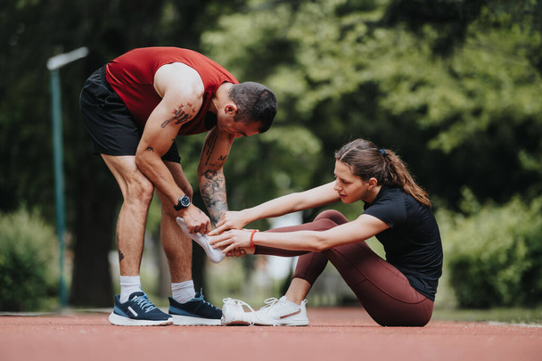 Un uomo in forma aiuta la sua ragazza con un infortunio alla gamba durante la loro corsa in un parco, mostrando supporto e preoccupazione. - Foto, immagini