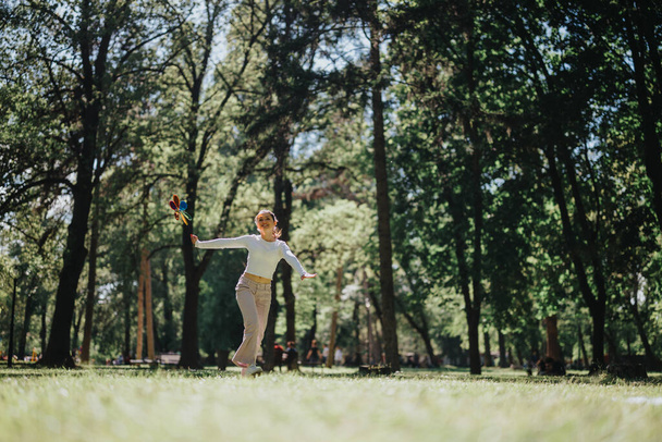 Capturada em um ambiente vibrante ao ar livre, esta imagem mostra uma jovem mulher brincando alegremente com um girador colorido em um exuberante parque verde sob o sol brilhante. - Foto, Imagem
