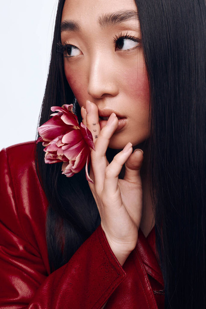 Portret van een vrouw met lang zwart haar en rood jasje met een bloem voor haar gezicht - Foto, afbeelding