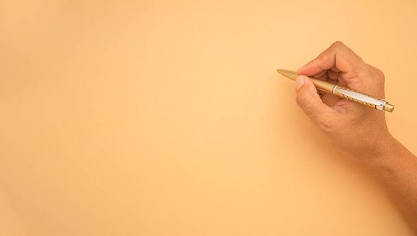 Κοντινό πλάνο της γυναίκας χέρι κρατώντας ένα στυλό σε ένα ανοιχτό πορτοκαλί χαρτί. Χώρος για κείμενο. Άνω όψη - Φωτογραφία, εικόνα