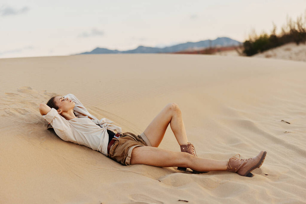 Frau entspannt sich in der Wüste mit den Beinen in der Luft und genießt die friedliche Einsamkeit der riesigen Sanddünen - Foto, Bild