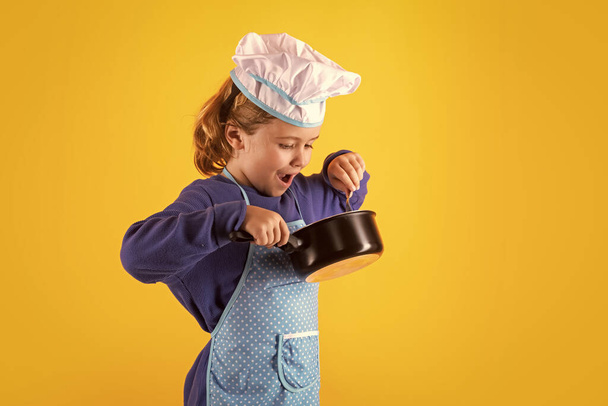 Kid chef cook with cooking pot stockpot. Cooking children. Chef kid boy in form of cook. Child boy with apron and chef hat preparing a healthy meal in the kitchen. Cooking process - Photo, image