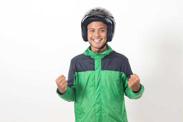 Retrato del taxista asiático en línea con chaqueta verde y casco levantando el puño, celebrando el éxito. Imagen aislada sobre fondo blanco - Foto, Imagen