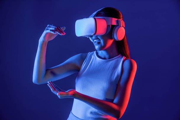 Smart Female staande omringd door neon licht dragen VR-headset aansluiten metaverse, futuristische cyberspace community technologie, met behulp van beide handen interactie met gegenereerd virtueel object. Hallucinatie. - Foto, afbeelding
