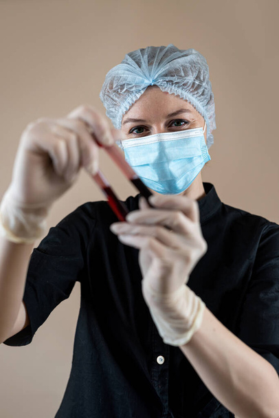 Белая женщина-учёный в чёрной форме держит пробирку для анализа крови, диагностические лаборатории - Фото, изображение