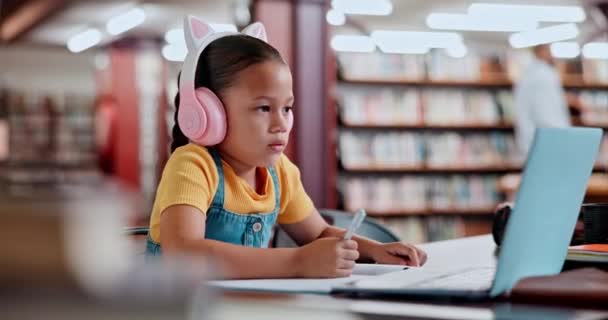 Laptop, headphones and student in library typing online for remote or distance learning on notebook. Technology, assessment and female child writing at school for elearning, studying or development. - Footage, Video
