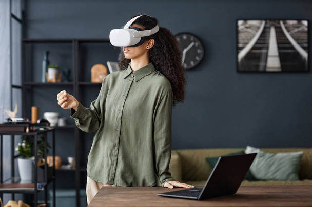 Mladá biracial žena nosí VR sluchátka stojící u stolu v obývacím pokoji doma surfování Internet, kopírovat prostor - Fotografie, Obrázek