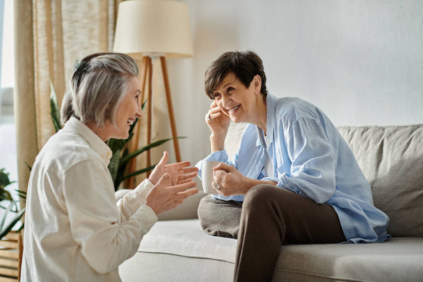 Two elderly women engaged in lively conversation on a cozy couch. - Photo, Image
