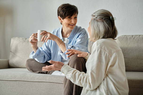 Milující starší lesbičky pár zapojit do hluboké konverzace, zatímco sedí na útulném gauči. - Fotografie, Obrázek