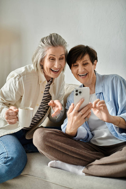 Dwie kobiety zajmują się telefonami siedząc na wygodnej kanapie. - Zdjęcie, obraz