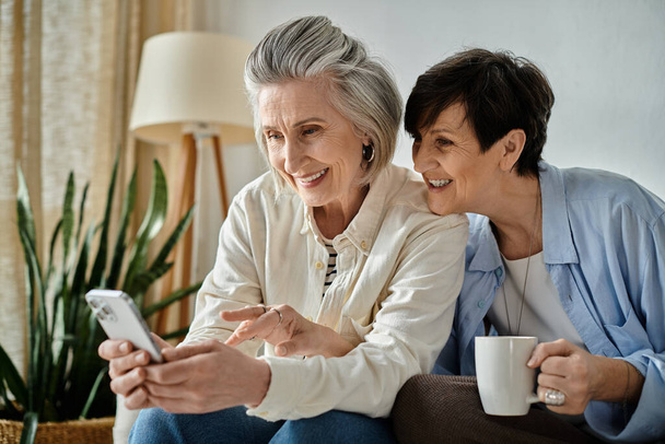 Zwei ältere Frauen auf einer Couch, in ein Handy vertieft. - Foto, Bild