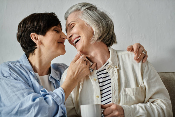 Two older women, a loving mature lesbian couple, share a cup of coffee on a cozy couch. - Photo, Image