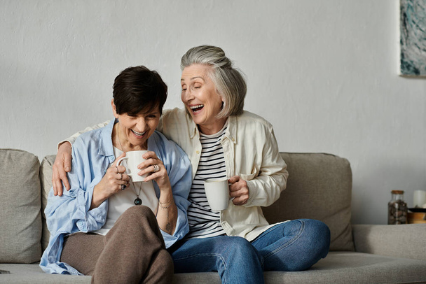 Zwei ältere Frauen genießen anmutig Kaffee auf einer gemütlichen Couch. - Foto, Bild