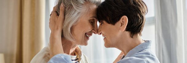 Zwei ältere Frauen umarmen sich vor einem Fenster liebevoll. - Foto, Bild