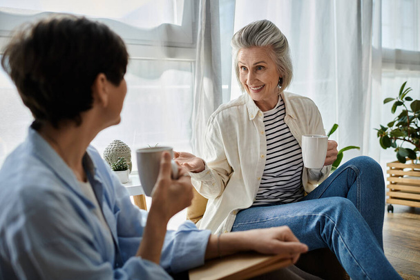 Dwie starsze kobiety rozmawiające na kanapie z kawą. - Zdjęcie, obraz