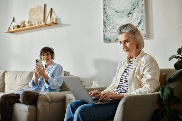 Две женщины наслаждаются уютным моментом на диване, занимаясь ноутбуком. - Фото, изображение